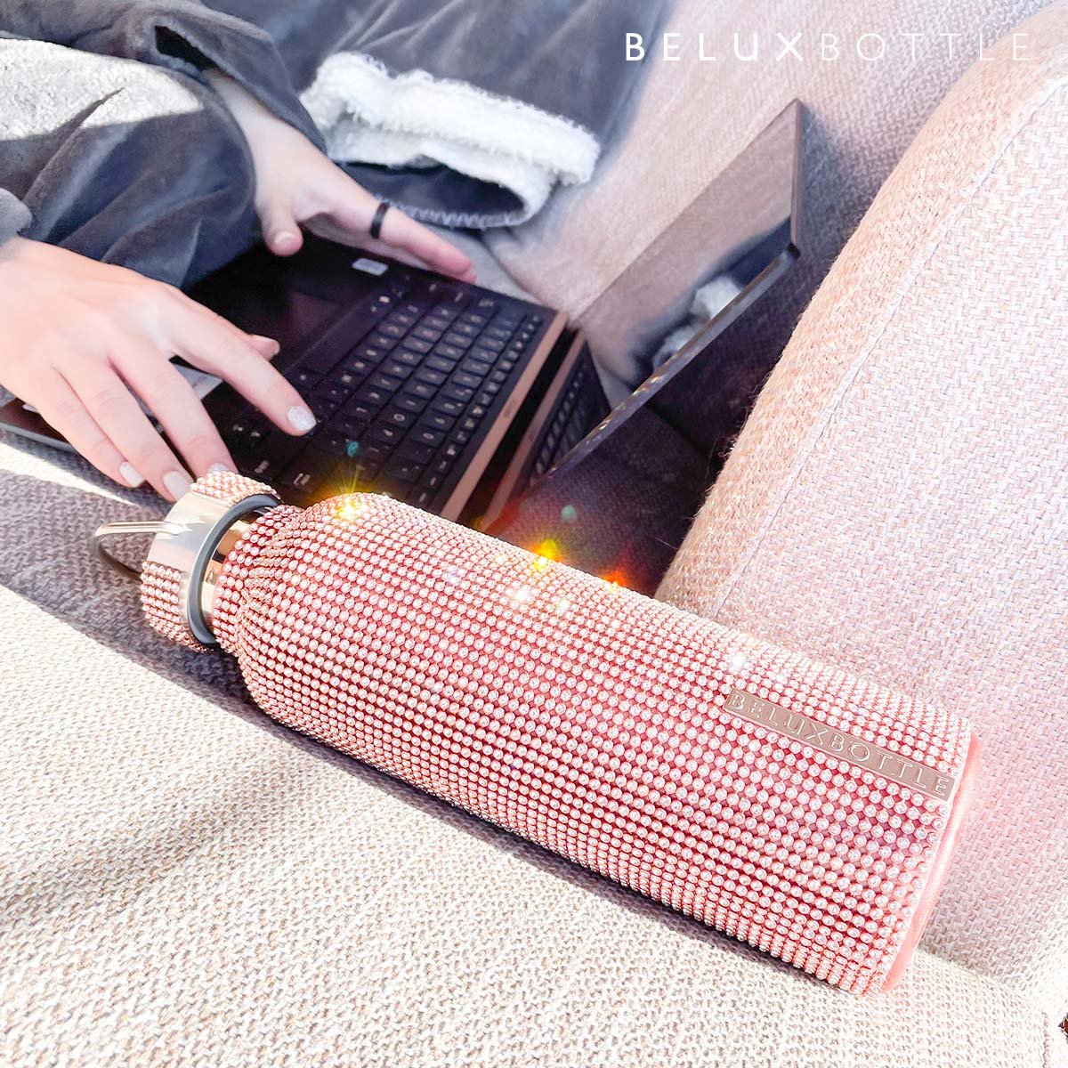 Rose Gold Sparkly Bling Bottle on beige couch, a girl working with laptop